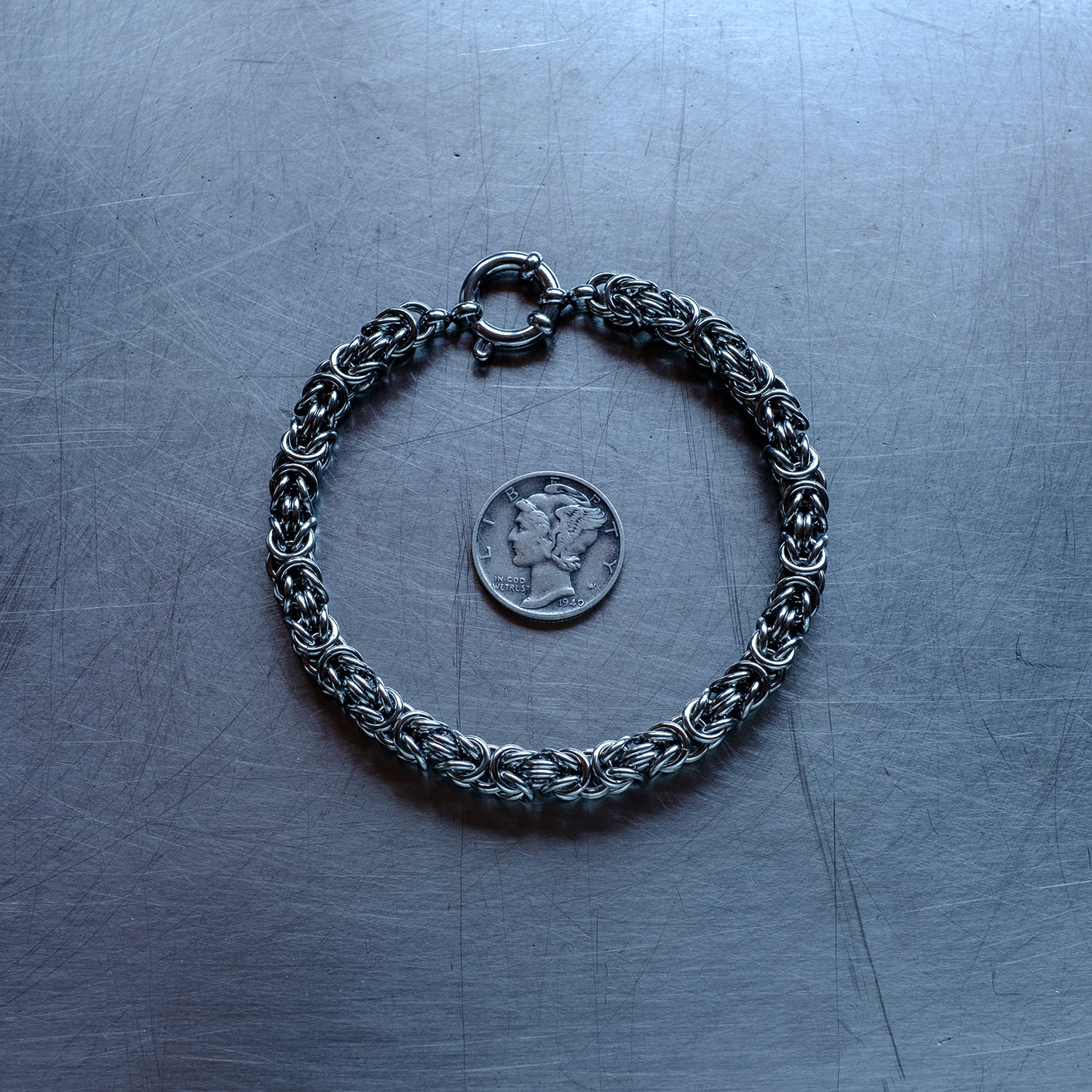 Classic in size, byzantine weave 304 stainless steel chain bracelet on a stainless steel surface with a liberty dime for scale