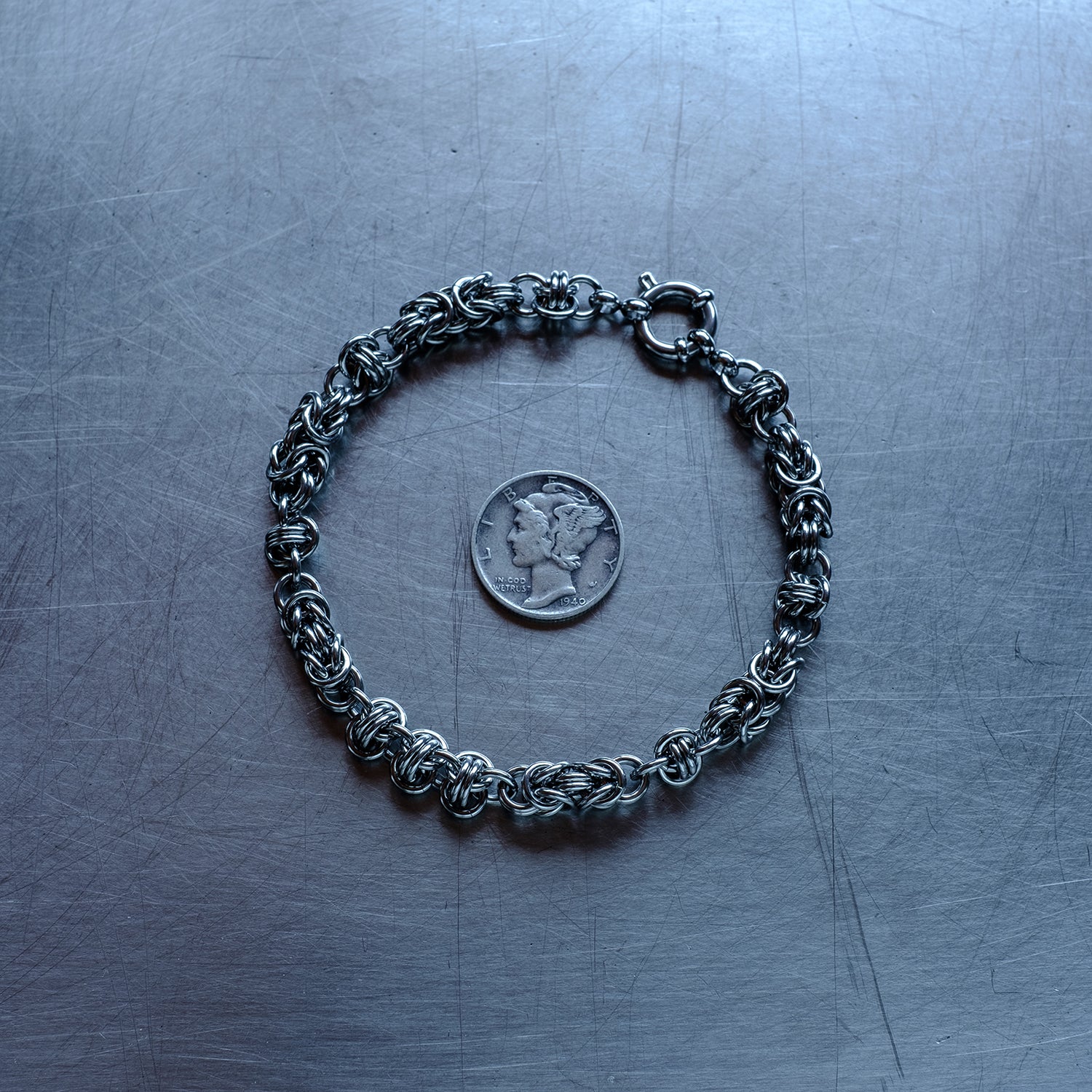 Classic in size, Byzantine and Barrel weave chain bracelet in alternating units configuration made with 304 stainless steel on a wet stainless steel surface with a quarter for scale