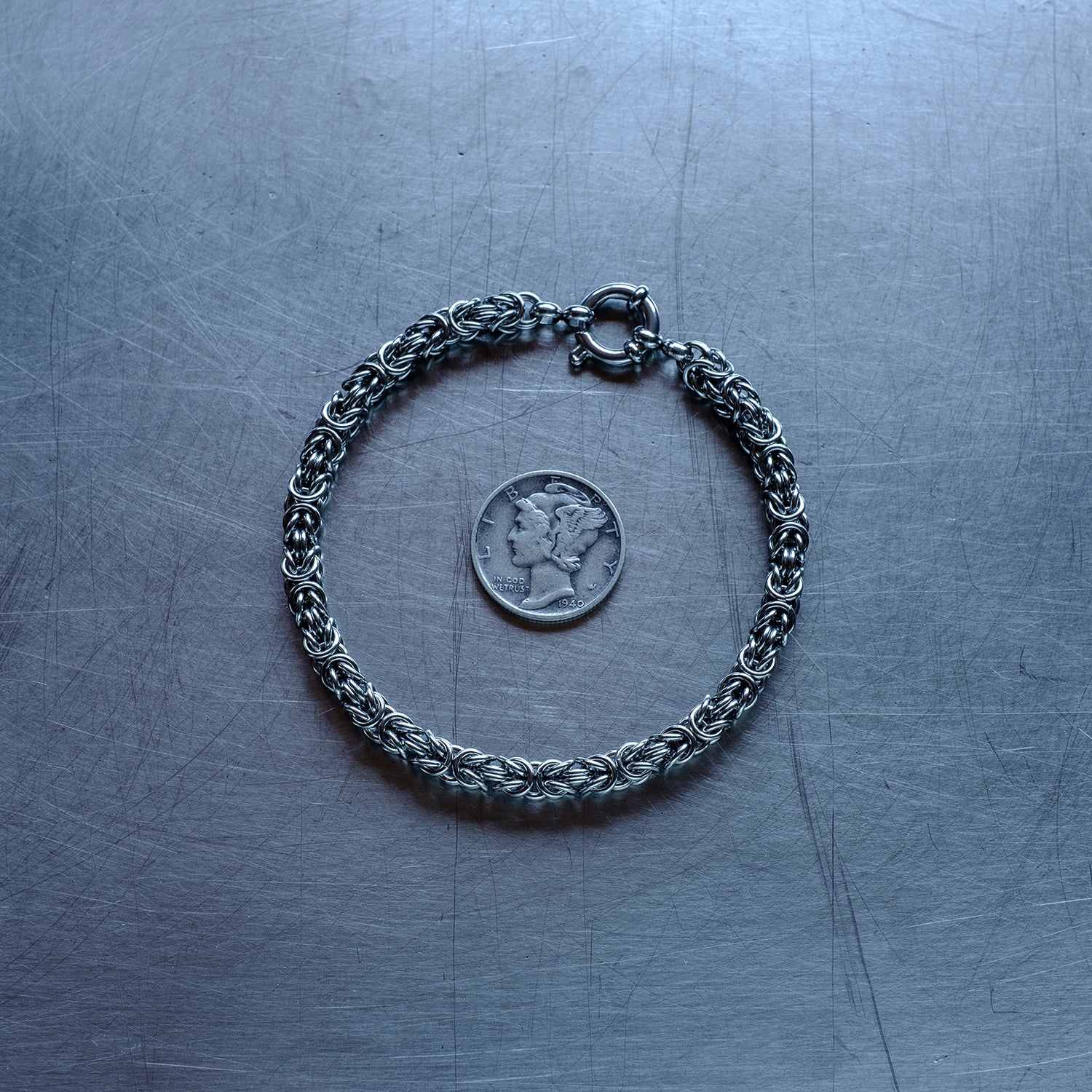 Dainty byzanatine weave chain Bracelet made of 304 stainless steel on stainless steel surface with a liberty dime for scale