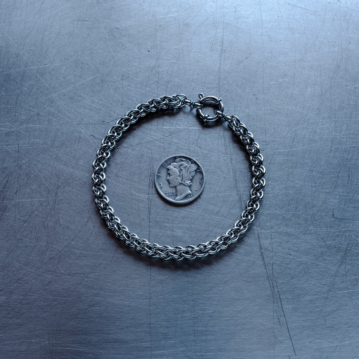 Dainty JPL3 weave chain bracelet made with 304 stainless steel on a stainless steel surface with a liberty dime for scale