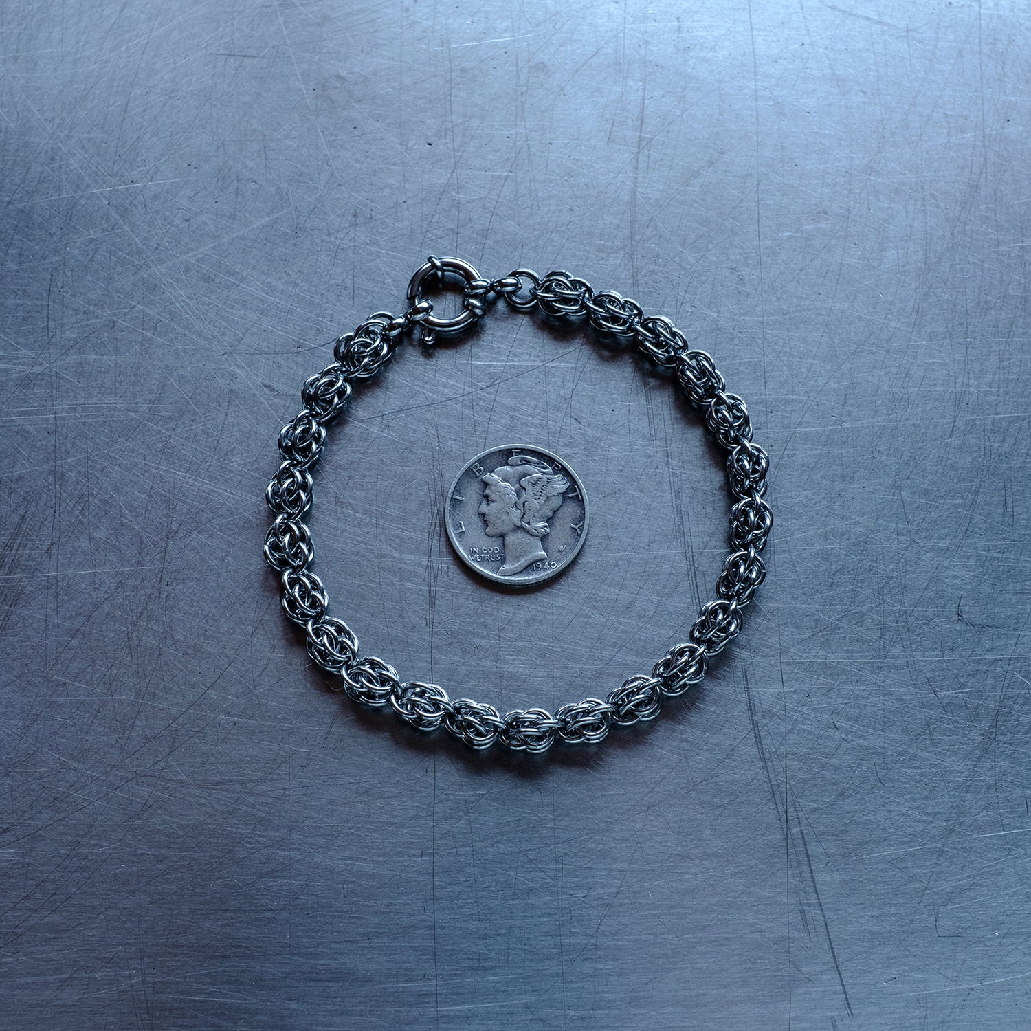 Dainty Sweet Pea weave chain bracelet made with 304 stainless steel on a stainless steel surface with a liberty dime for scale