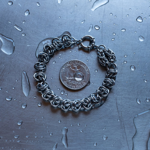 Bold Barrel weave with Byzantine Head Snake chain bracelet made with 304 stainless steel on a wet stainless steel surface with a quarter for scale