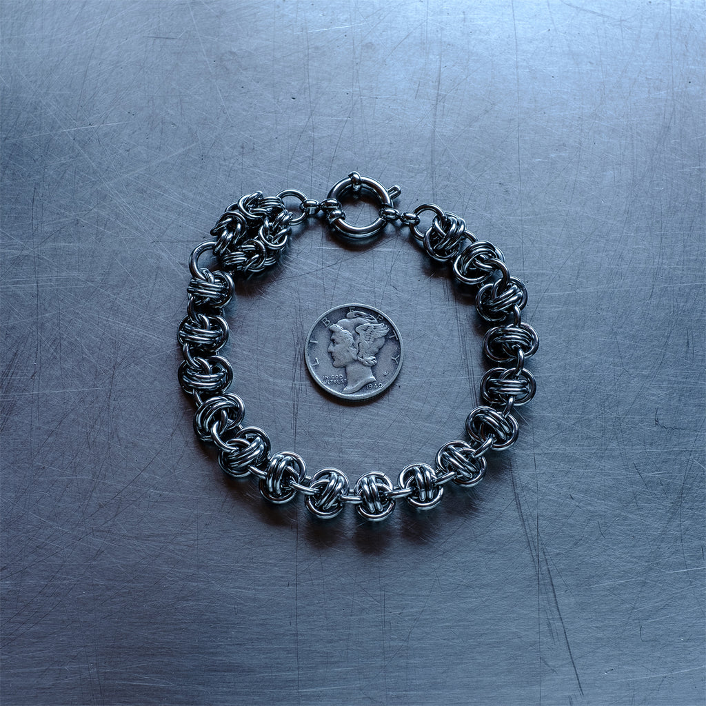 Bold Barrel weave with Byzantine Head Snake chain bracelet made with 304 stainless steel on a stainless steel surface with a liberty dime for scale