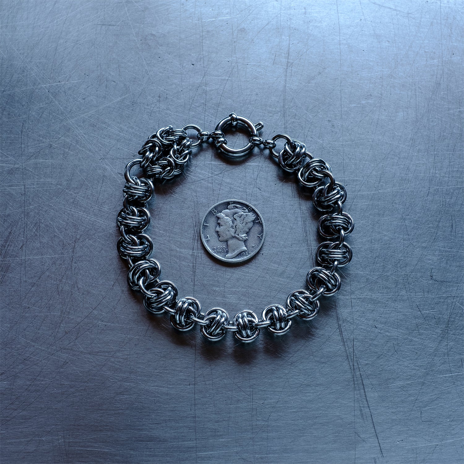 Bold Barrel weave with Byzantine Head Snake chain bracelet made with 304 stainless steel on a stainless steel surface with a liberty dime for scale