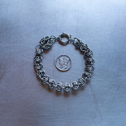 Bold Barrel weave with Byzantine Head Snake chain bracelet made with 304 stainless steel on a stainless steel surface with a liberty dime for scale