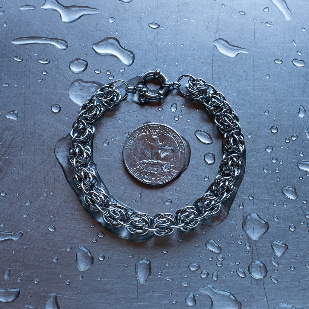 Bold bipolar beestings weave chain bracelet made with 304 stainless steel on a wet stainless steel surface with a quarter for scale.