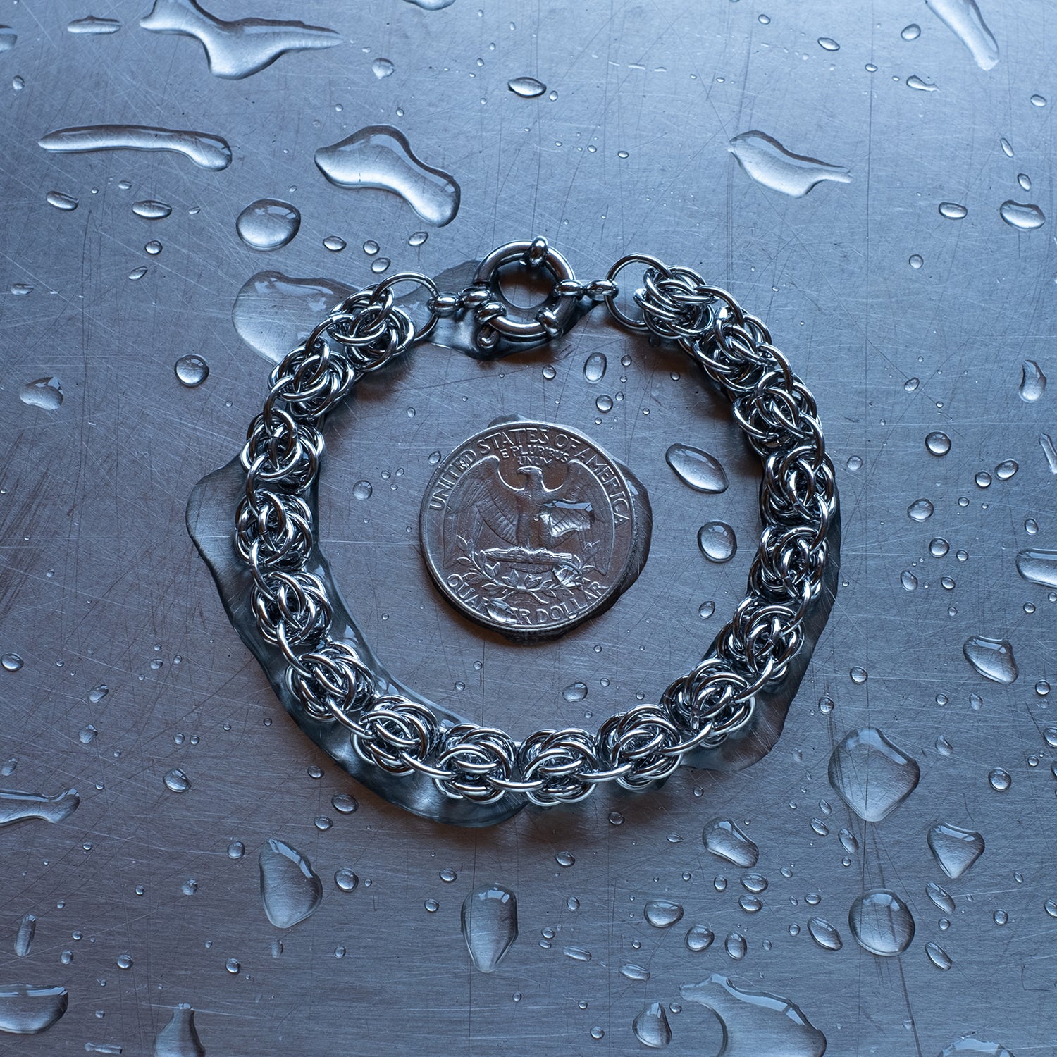Bold bipolar beestings weave chain bracelet made with 304 stainless steel on a wet stainless steel surface with a quarter for scale.