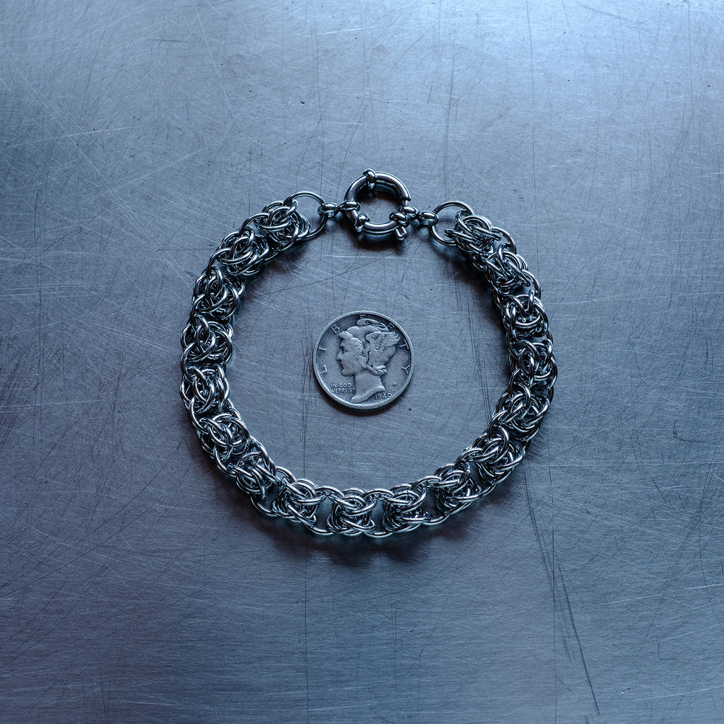 Bold bipolar beestings weave chain bracelet made with 304 stainless steel on a stainless steel surface with a liberty dime for scale.
