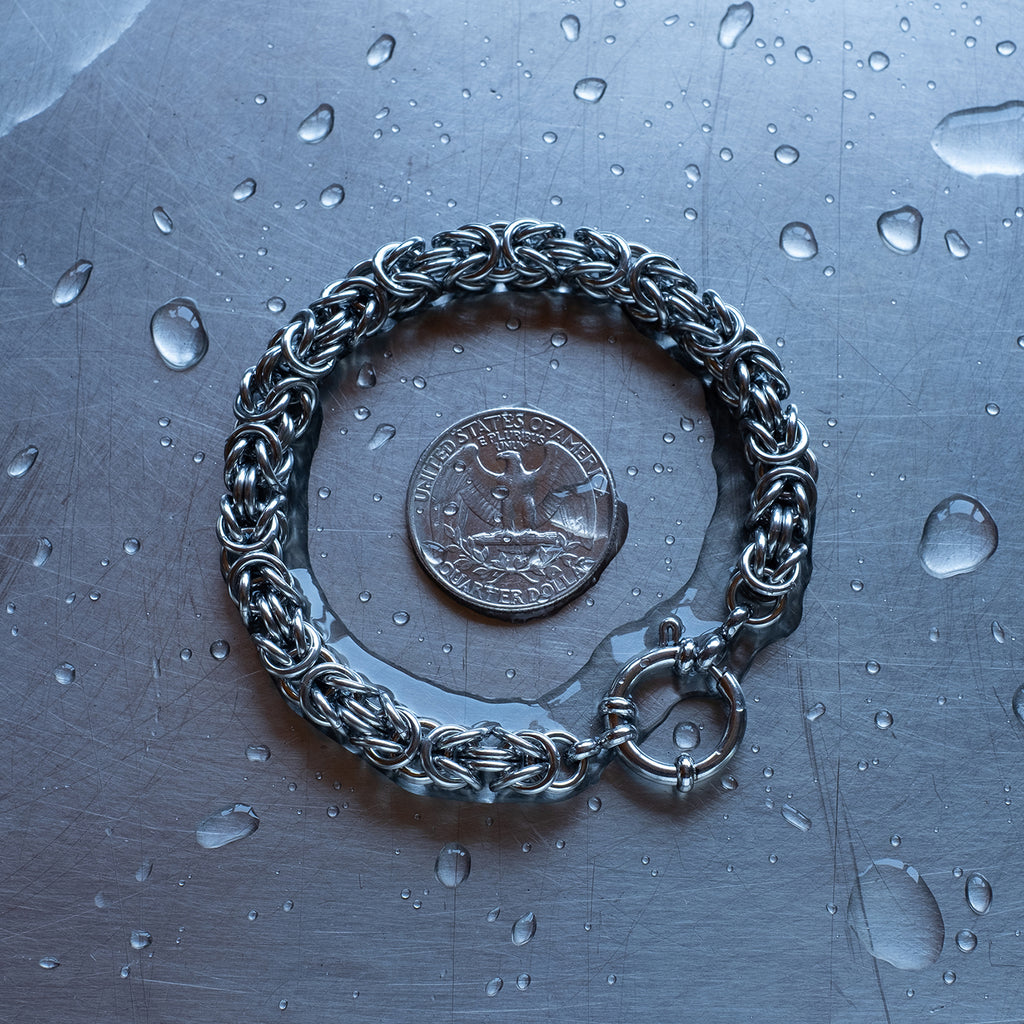 Bold byzantine weave 304 stainless steel chain bracelet on a stainless steel surface with a quarter for scale