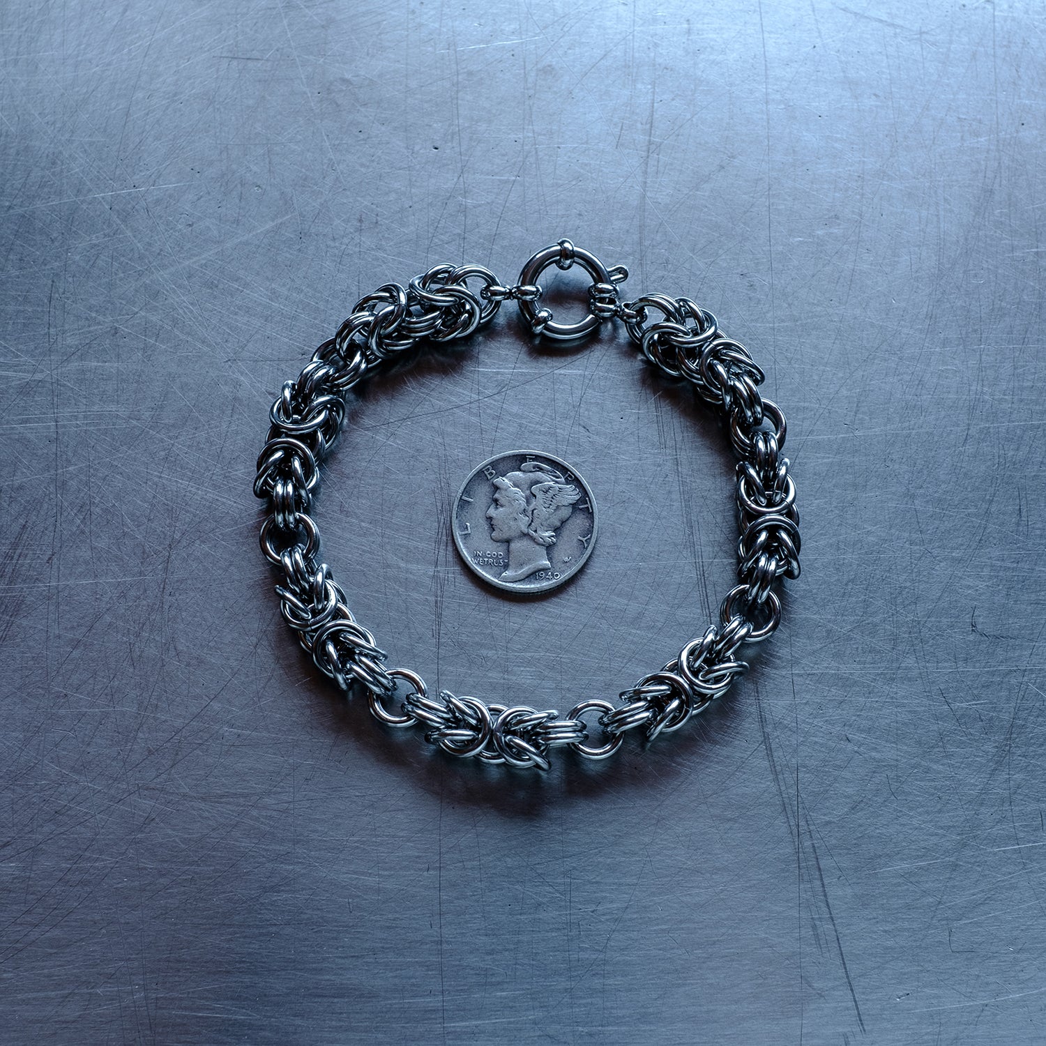 Bold Byzantine weave chain bracelet in units configuration made with 304 stainless steel on a stainless steel surface with a liberty dime for scale