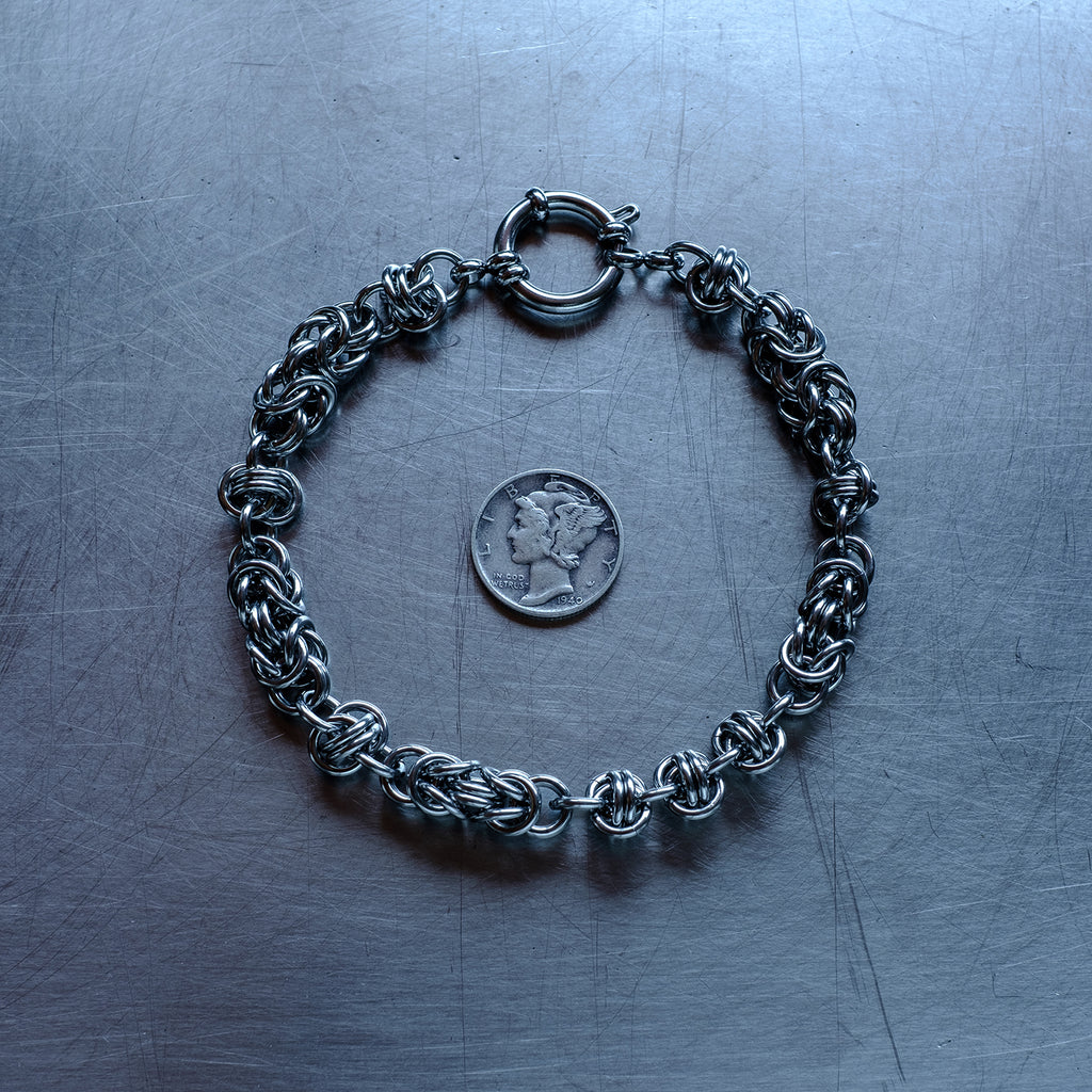 Bold Byzantine and Barrel weave chain bracelet in alternating units configuration made with 304 stainless steel on a stainless steel surface with a liberty dime for scale