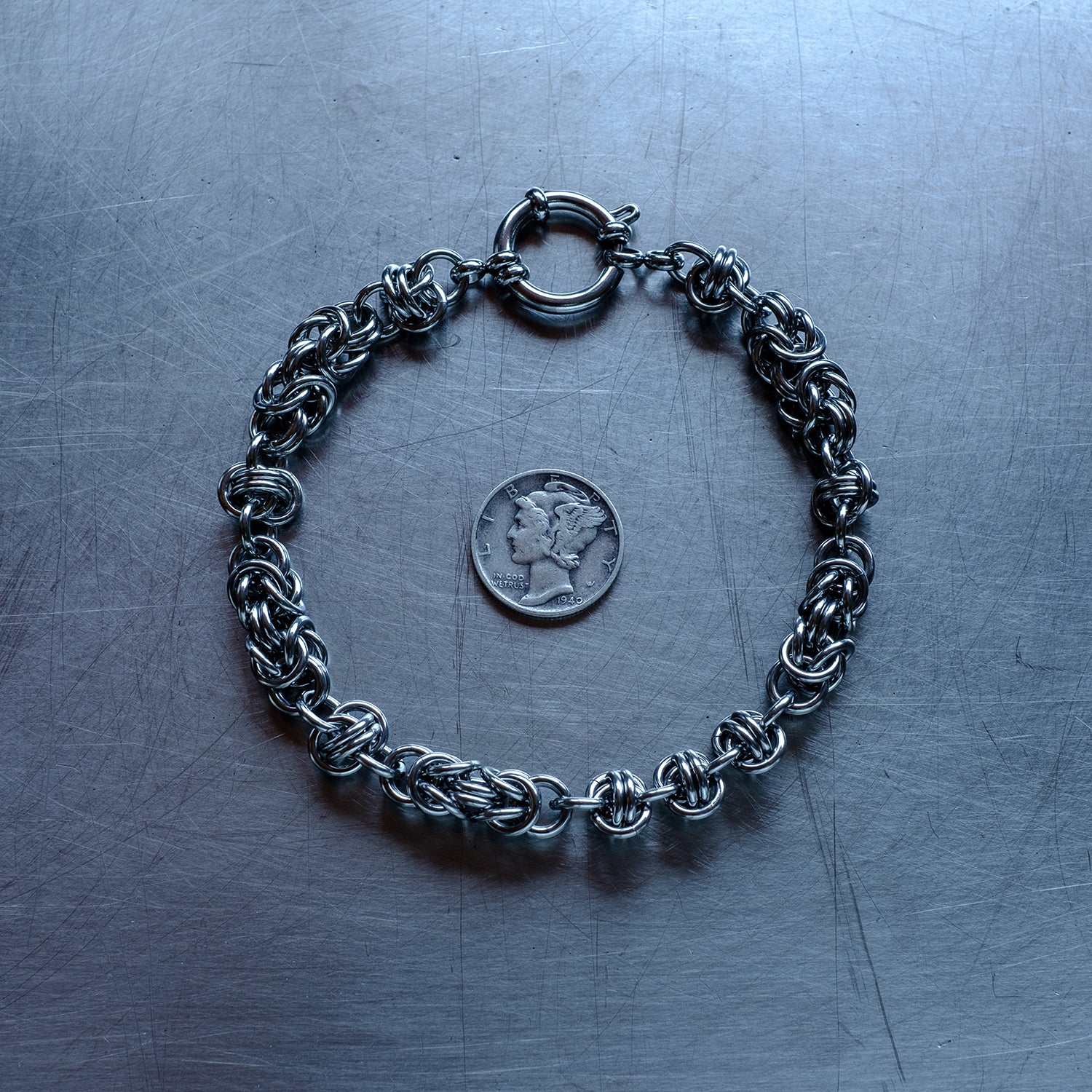 Bold Byzantine and Barrel weave chain bracelet in alternating units configuration made with 304 stainless steel on a stainless steel surface with a liberty dime for scale