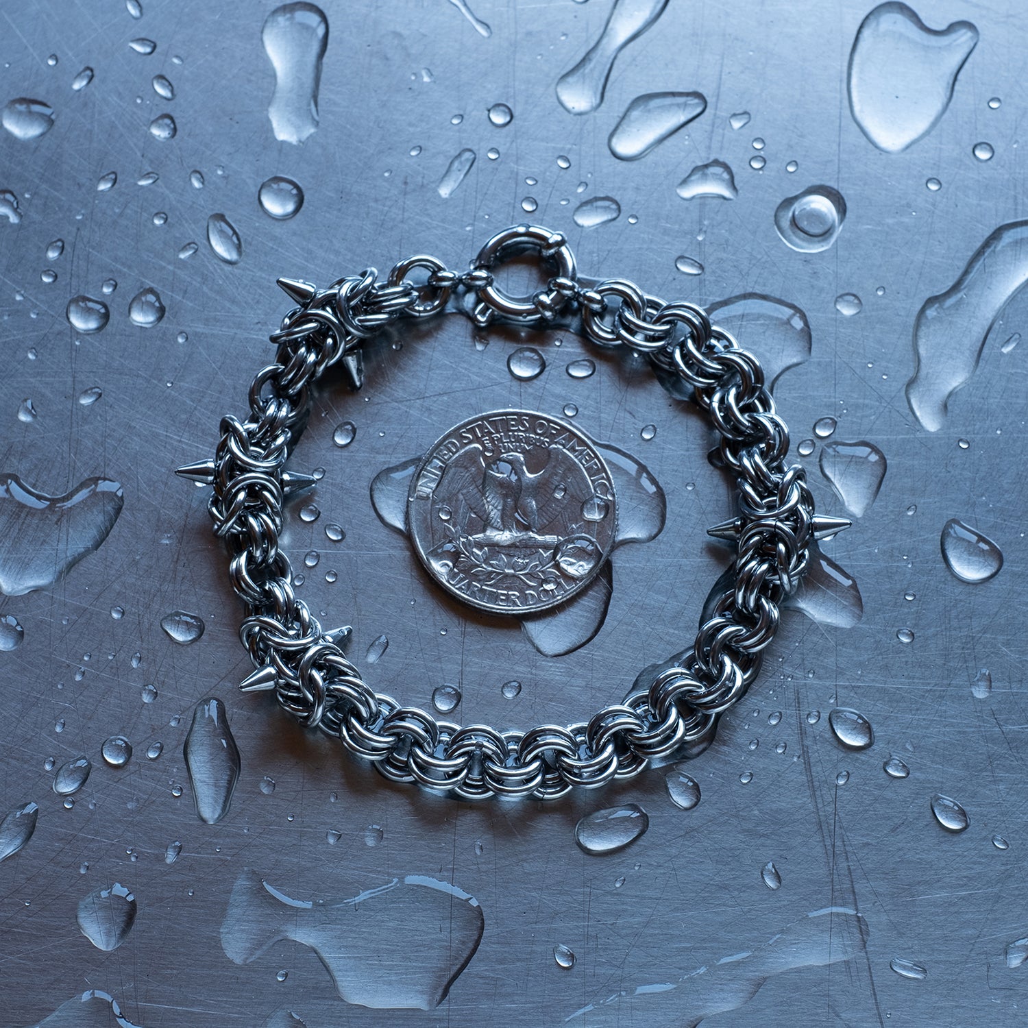 Bold, sections of Byzantine weave with spikes and 2 in 1 weave, chain bracelet with medieval vibes made with 304 stainless steel on a wet stainless steel surface with a quarter for scale