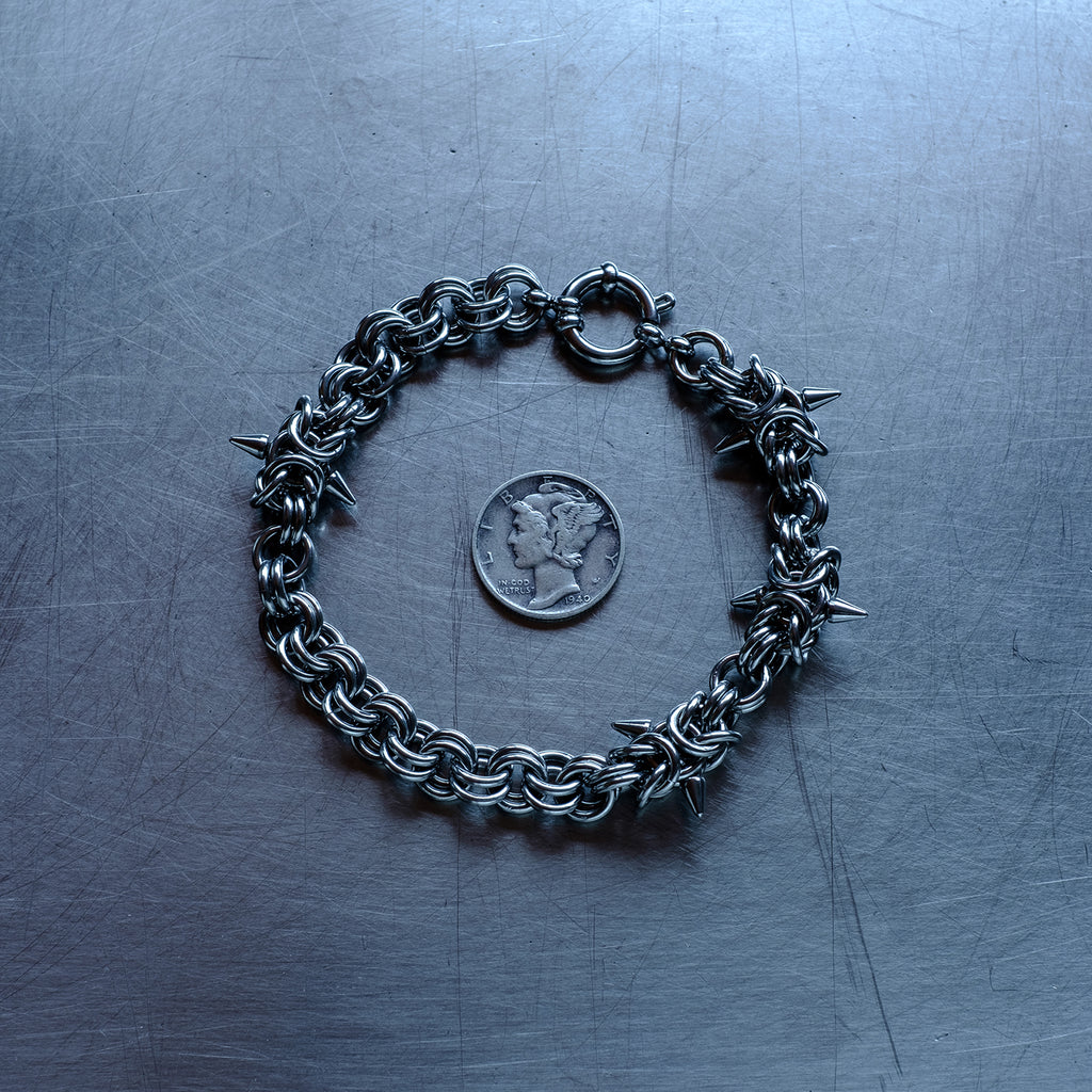 Bold, sections of Byzantine weave with spikes and 2 in 1 weave, chain bracelet with medieval vibes made with 304 stainless steel on a stainless steel surface with a liberty dime for scale