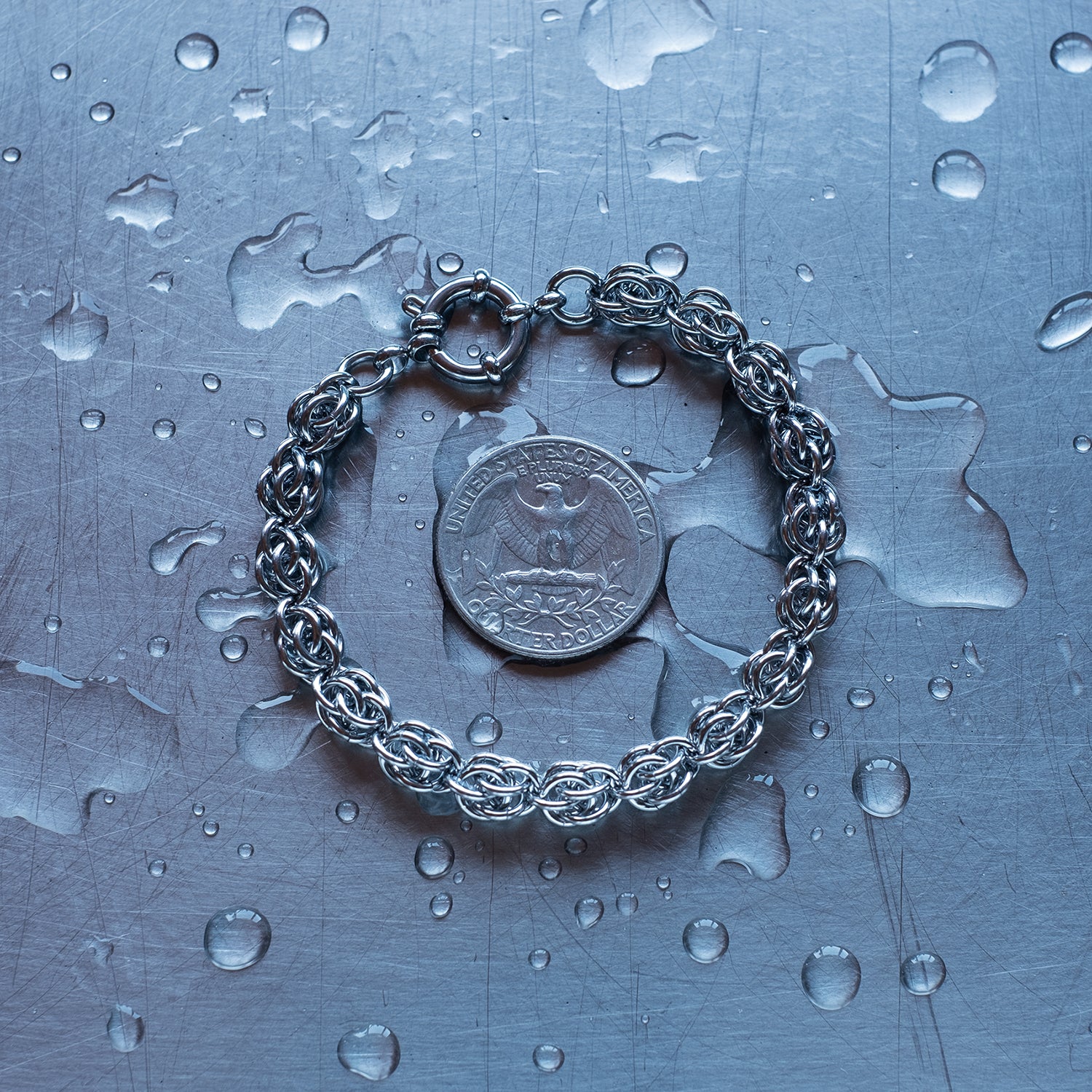 Classic Sweet Pea weave chain bracelet made with 304 stainless steel on a wet stainless steel surface with a quarter for scale