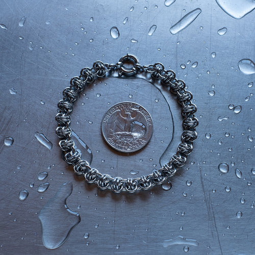 Classic in size, Barrel weave chain bracelet made with 304 stainless steel on a wet stainless steel surface with a quarter for scale