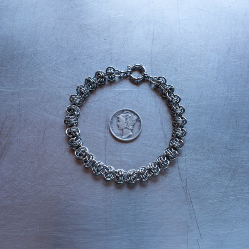 Classic in size, Barrel weave chain bracelet made with 304 stainless steel on a stainless steel surface with a liberty dime for scale