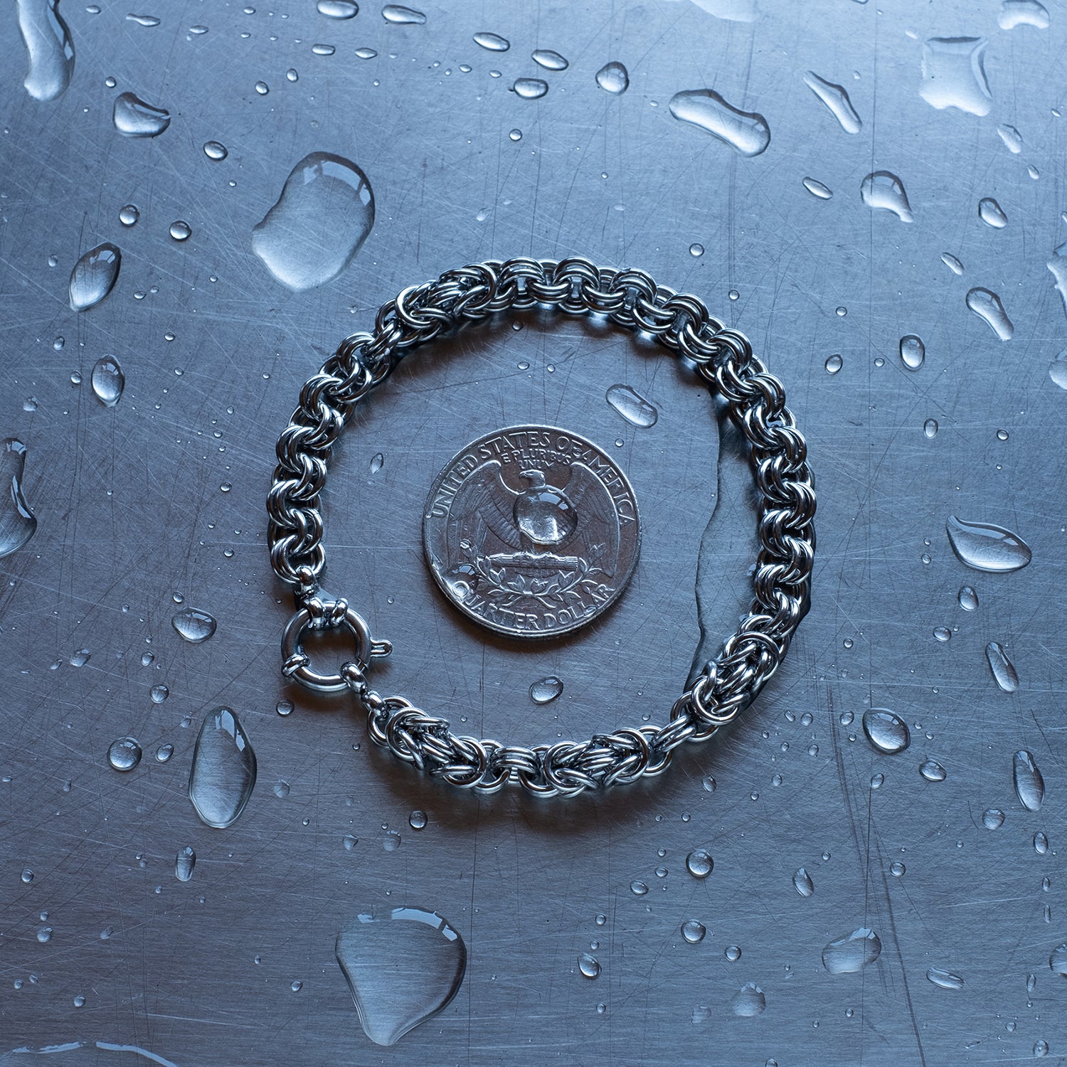 Classic in size, Byzantine Units offset and alternating with 2 in 1 weave chain bracelet made with 304 stainless steel on a wet stainless steel surface with a quarter for scale
