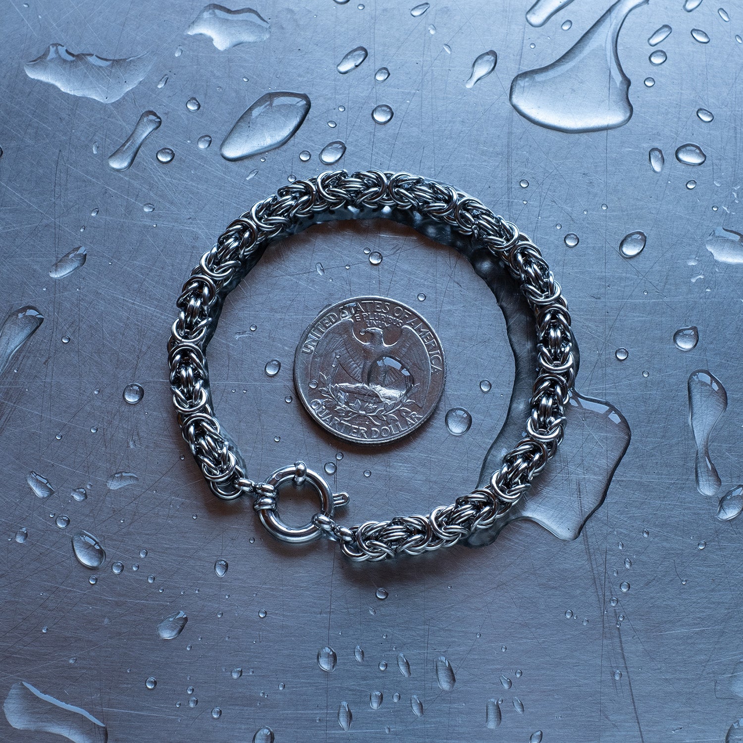 Classic in size, byzantine weave 304 stainless steel chain bracelet on a wet stainless steel surface with a quarter for scale