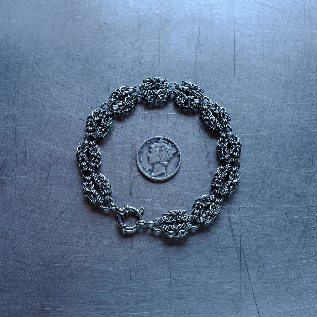 Classic in size byzantine weave bracelet in "heads" configuration made of 304 stainless steel chain bracelet on a stainless steel surface with a quarter for scale