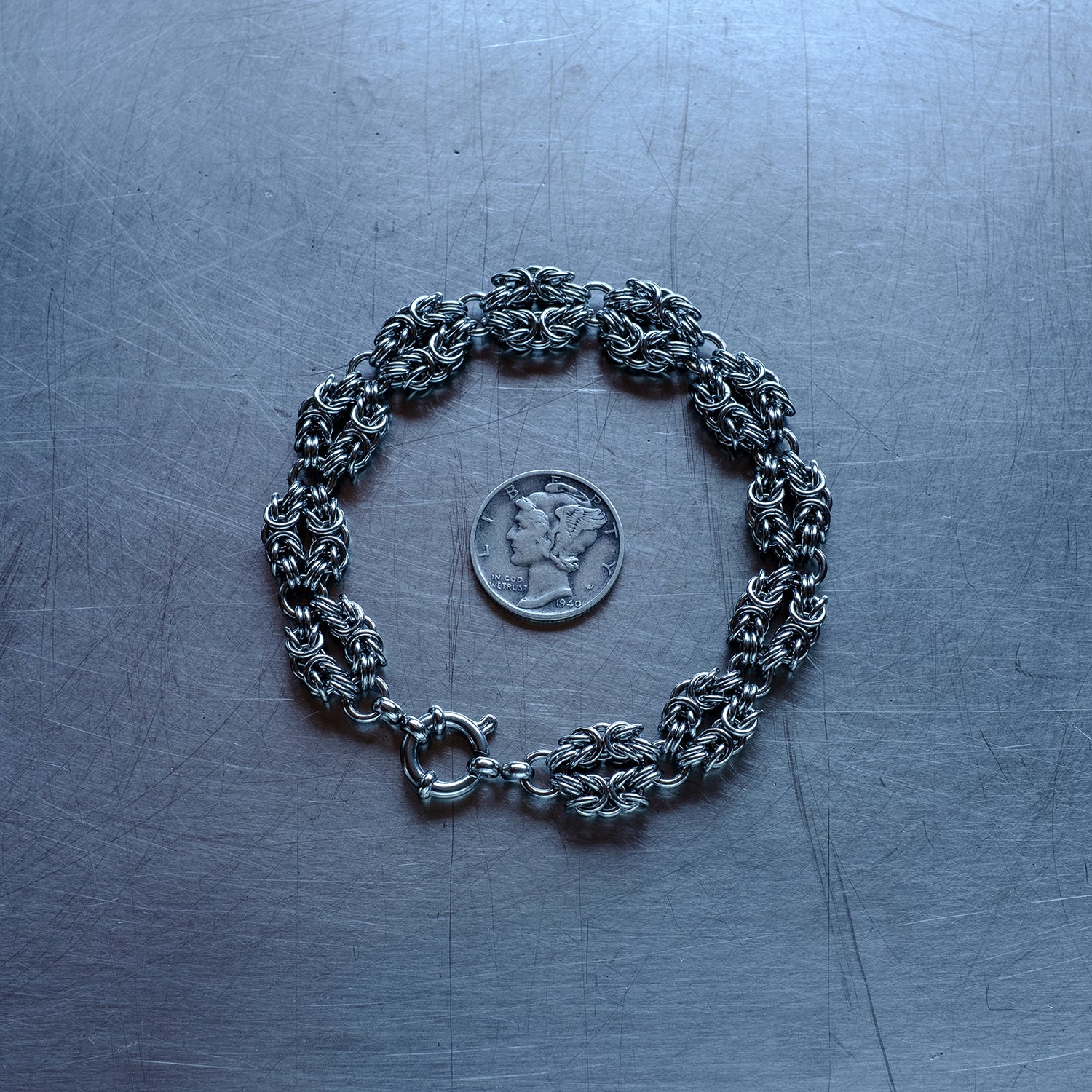 Classic in size byzantine weave bracelet in "heads" configuration made of 304 stainless steel chain bracelet on a stainless steel surface with a quarter for scale