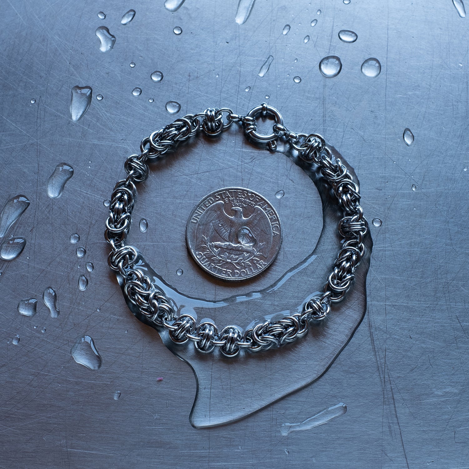 Classic in size, Byzantine and Barrel weave chain bracelet in alternating units configuration made with 304 stainless steel on a wet stainless steel surface with a quarter for scale