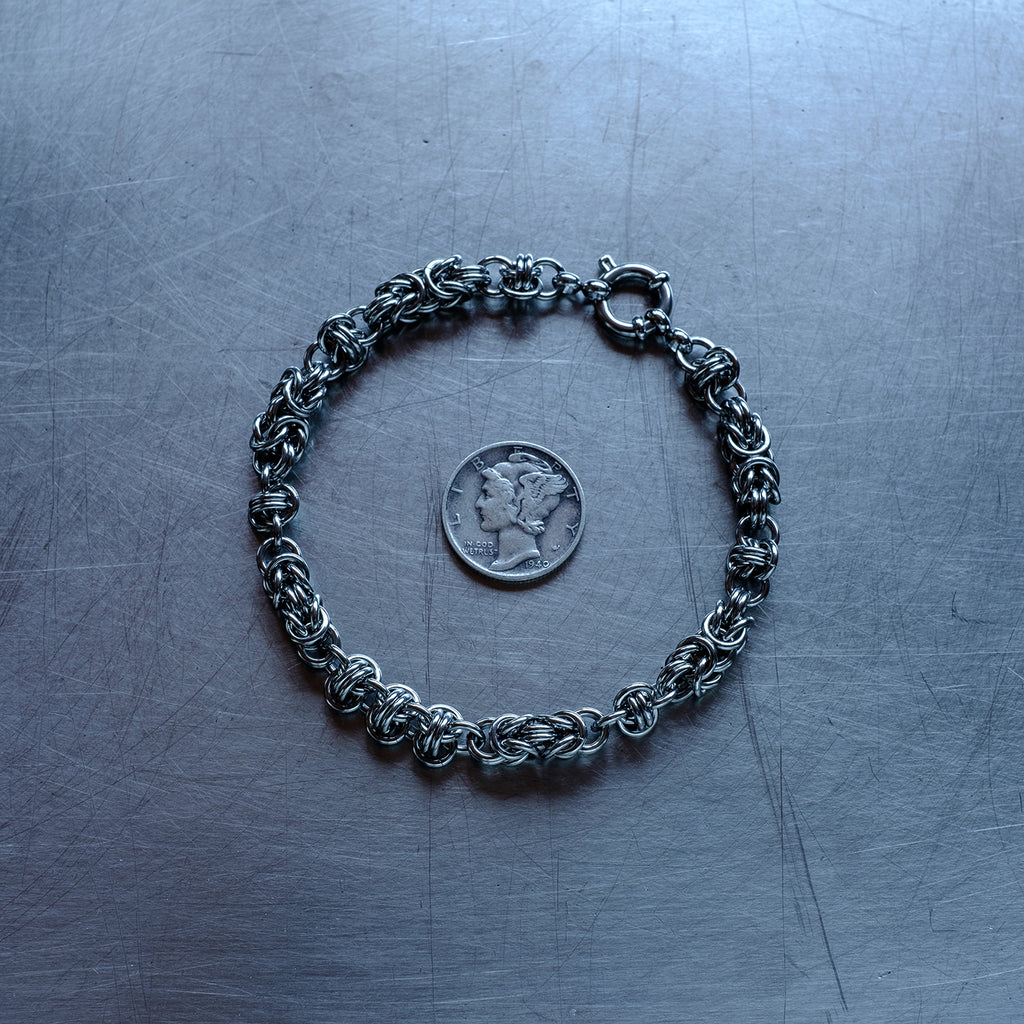 Classic in size, Byzantine and Barrel weave chain bracelet in alternating units configuration made with 304 stainless steel on a wet stainless steel surface with a quarter for scale