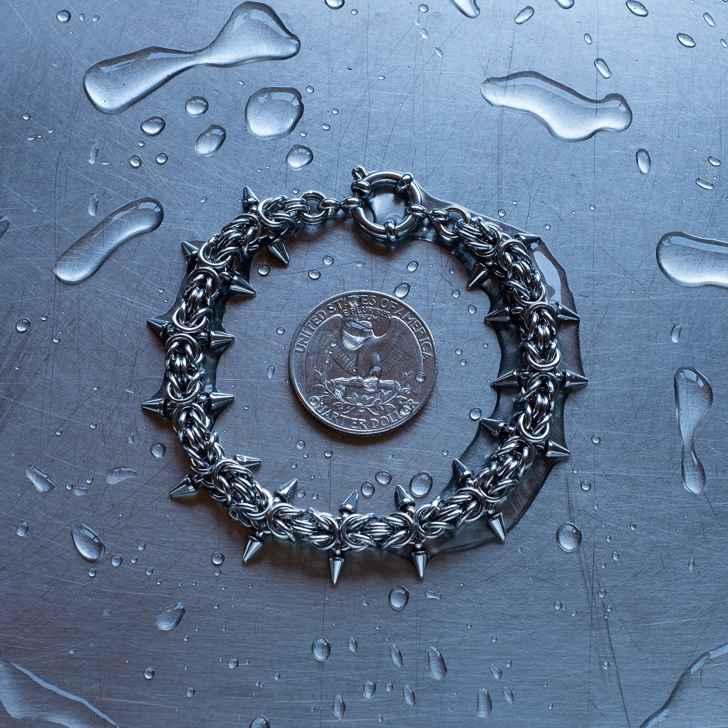 Classic in size, Spikey Byzantine weave chain bracelet made with 304 stainless steel on a wet stainless steel surface with a quarter for scale