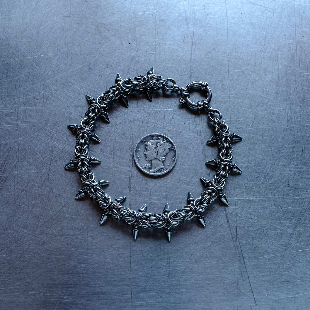 Classic in size, Spikey Byzantine weave chain bracelet made with 304 stainless steel on a stainless steel surface with a liberty dime for scale