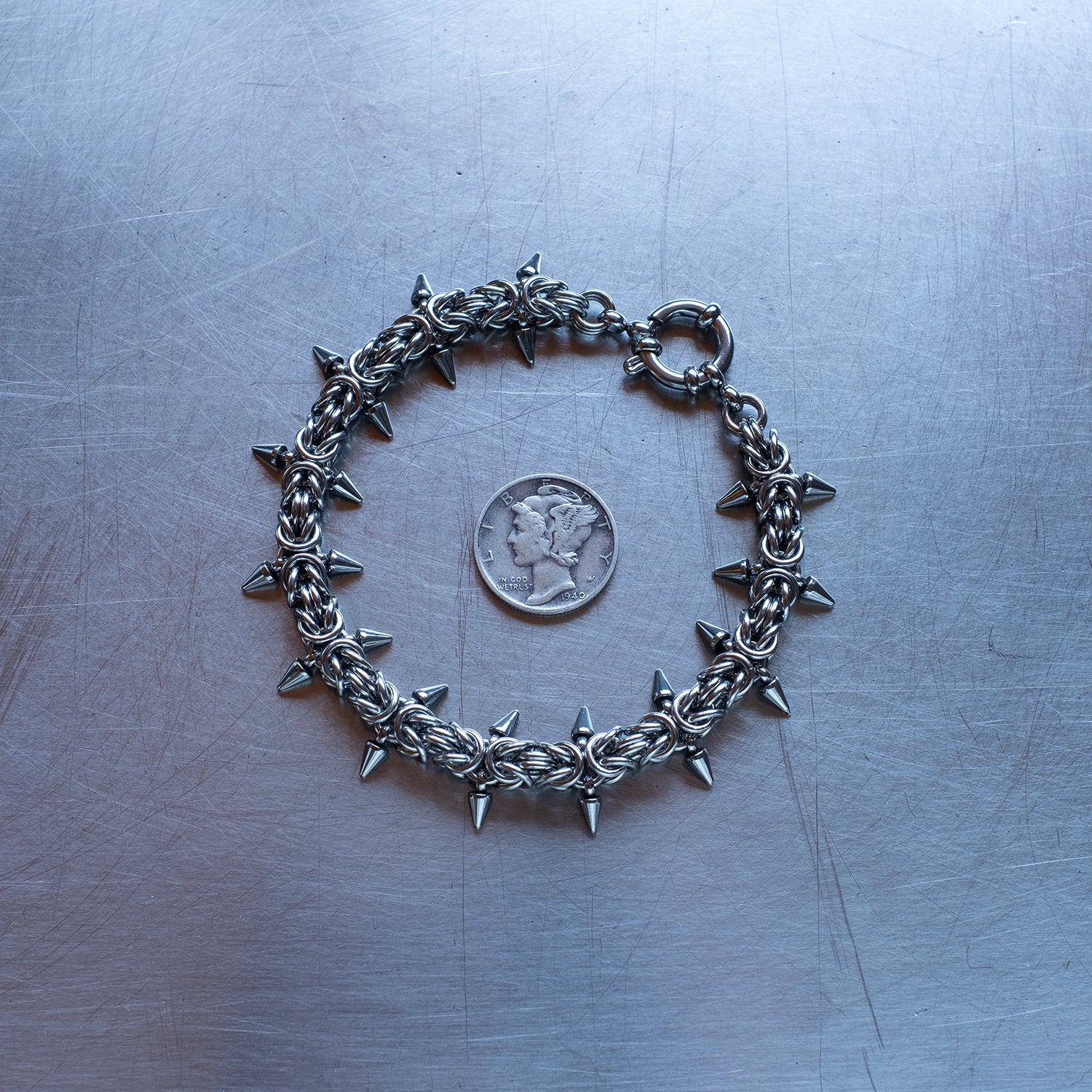 Classic in size, Spikey Byzantine weave chain bracelet made with 304 stainless steel on a stainless steel surface with a liberty dime for scale