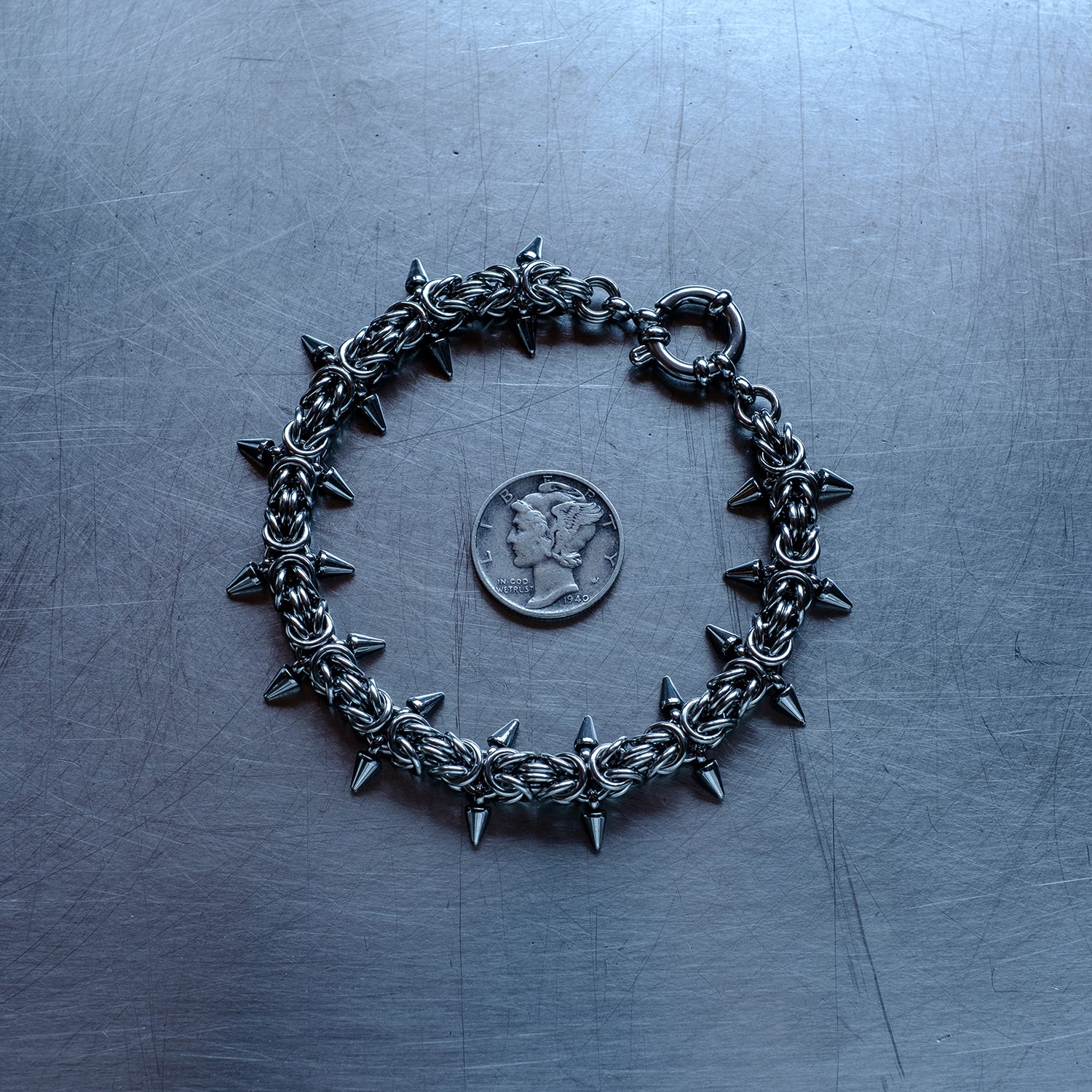 Classic in size, Spikey Byzantine weave chain bracelet made with 304 stainless steel on a stainless steel surface with a liberty dime for scale