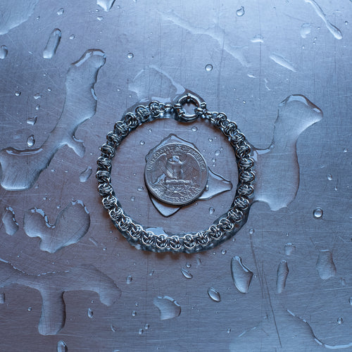 Dainty, Barrel weave 304 stainless steel chain bracelet on a stainless steel surface with a quarter for scale