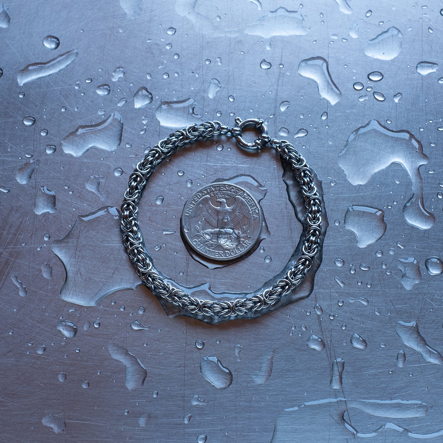 Dainty, byzantine weave 304 stainless steel chain bracelet on a stainless steel surface with a quarter for scale