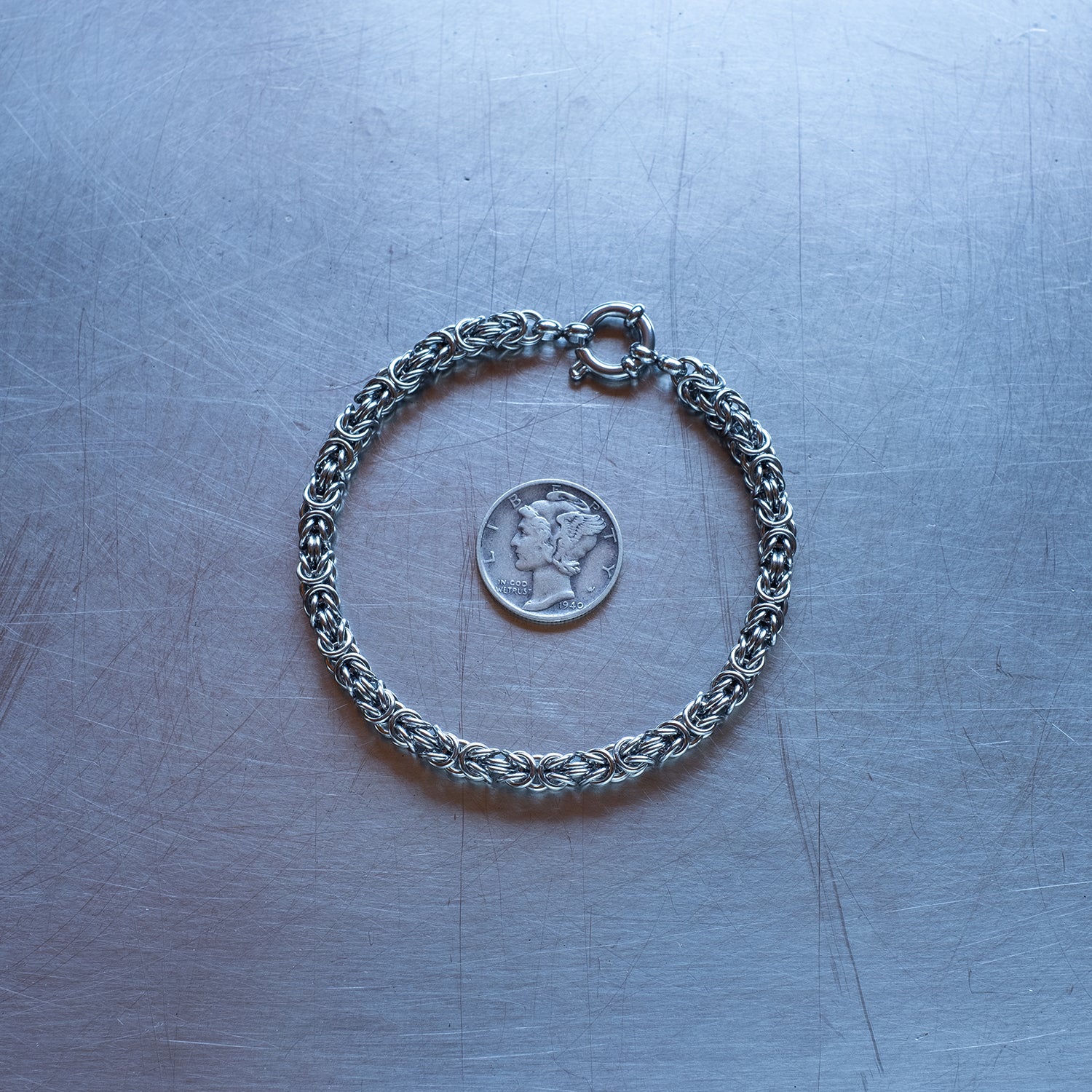 Dainty byzanatine weave chain Bracelet made of 304 stainless steel on stainless steel surface with a liberty dime for scale