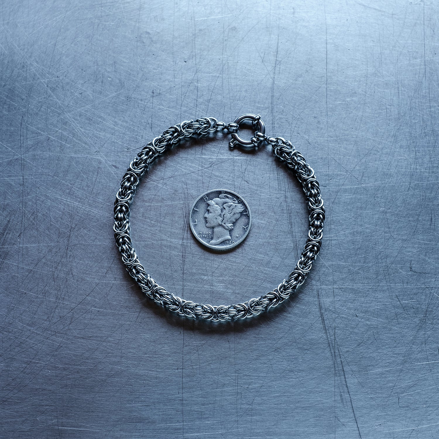 Dainty byzanatine weave chain Bracelet made of 304 stainless steel on stainless steel surface with a liberty dime for scale