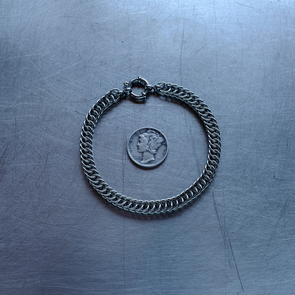 Dainty, Half persian weave chain bracelet made with 304 stainless steel on a stainless steel surface with a liberty dime for scale