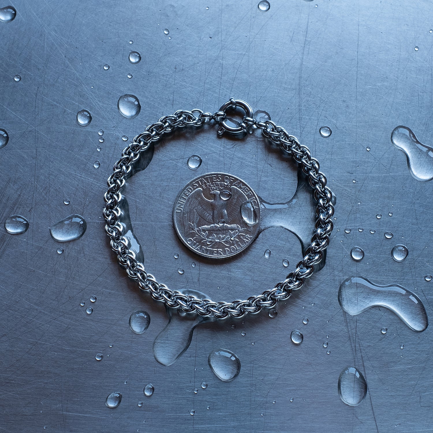 Dainty JPL3 weave chain bracelet made with 304 stainless steel on a wet stainless steel surface with a quarter for scale