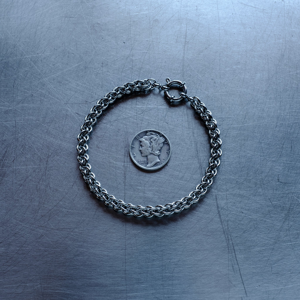 Dainty JPL3 weave chain bracelet made with 304 stainless steel on a stainless steel surface with a liberty dime for scale