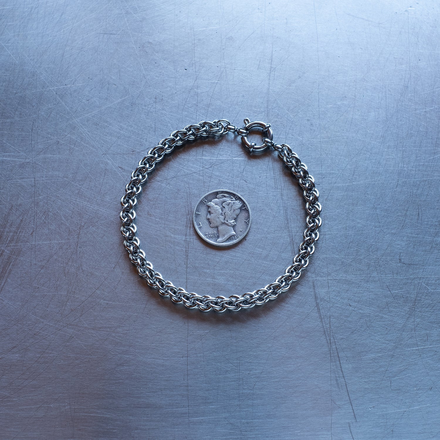 Dainty JPL3 weave chain bracelet made with 304 stainless steel on a stainless steel surface with a liberty dime for scale