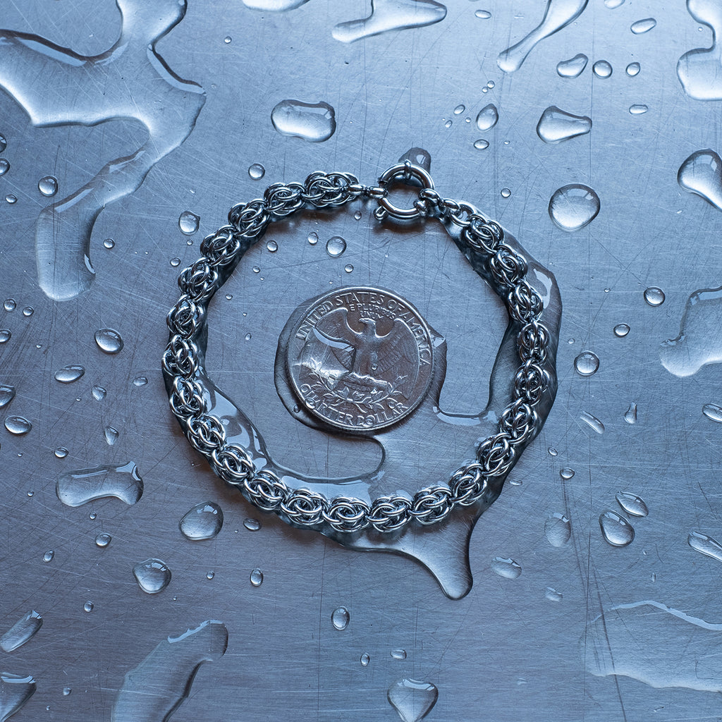Dainty Sweet Pea weave chain bracelet made with 304 stainless steel on a wet stainless steel surface with a quarter for scale