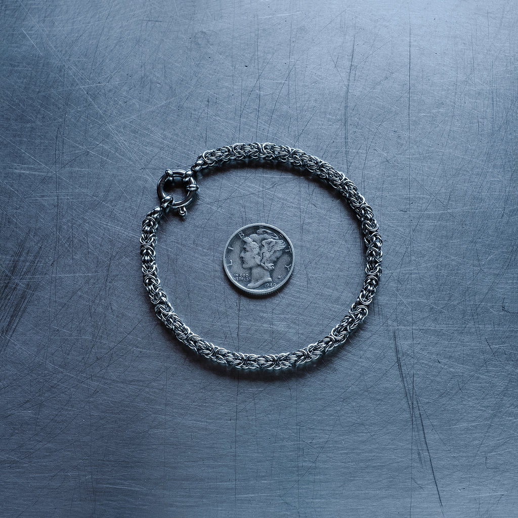 fine byzantine weave chain bracelet made with 304 stainless steel on a stainless steel surface with a liberty dime for scale