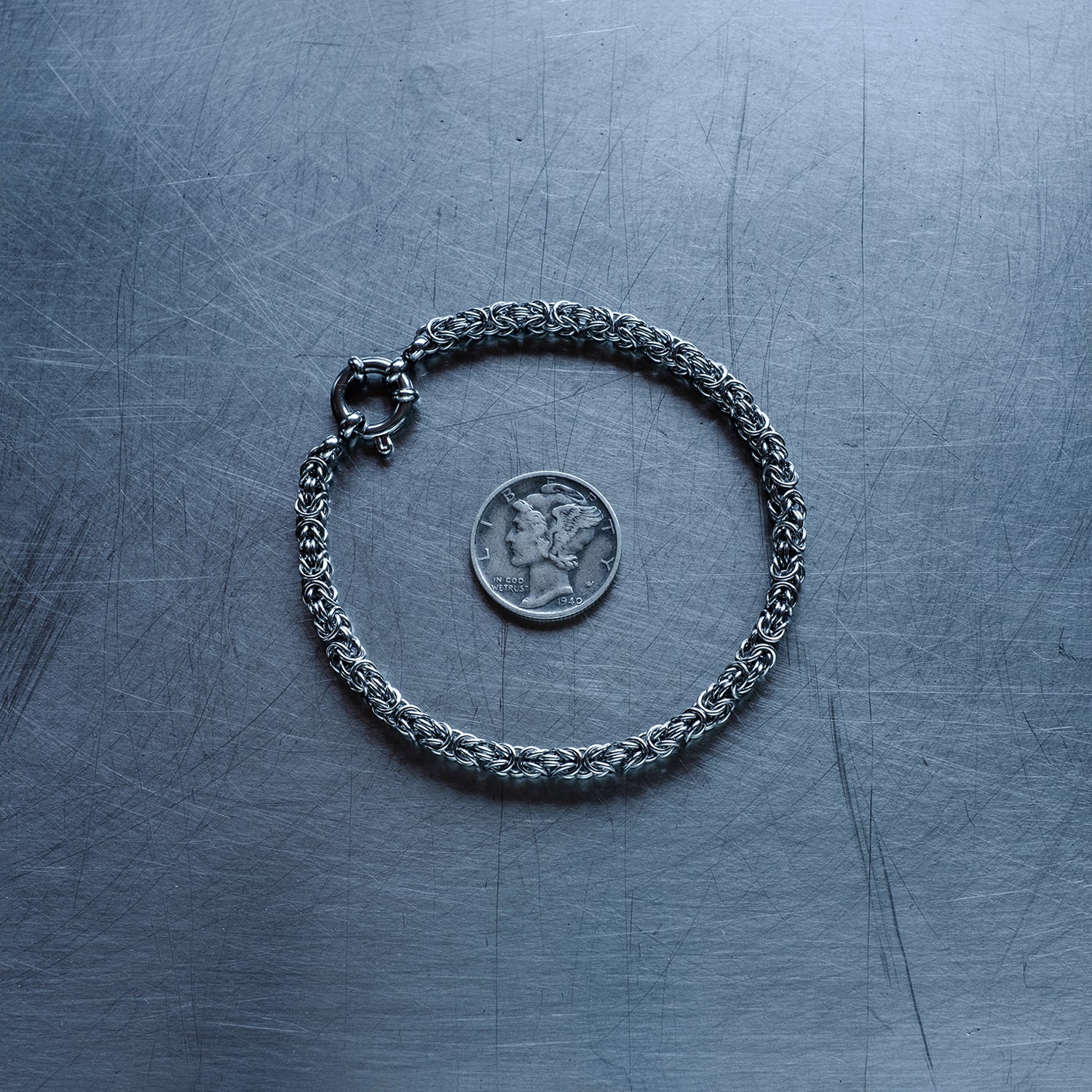 fine byzantine weave chain bracelet made with 304 stainless steel on a stainless steel surface with a liberty dime for scale