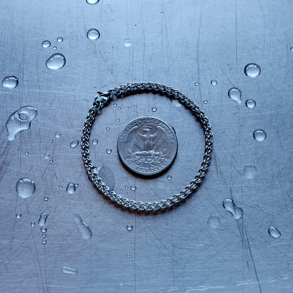 fine jpl3 weave chain bracelet made with 304 stainless steel on a wet stainless steel surface with a quarter for scale