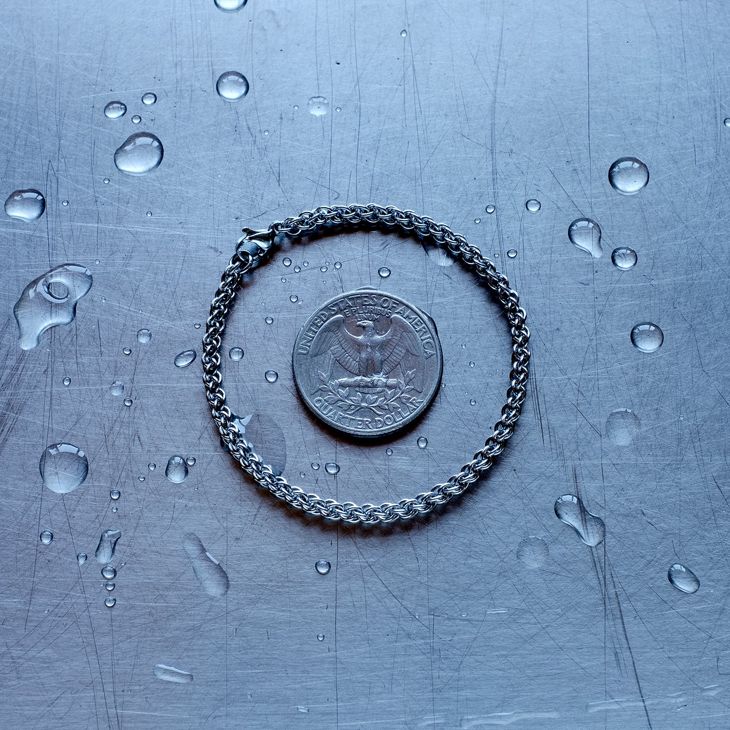 fine jpl3 weave chain bracelet made with 304 stainless steel on a wet stainless steel surface with a quarter for scale
