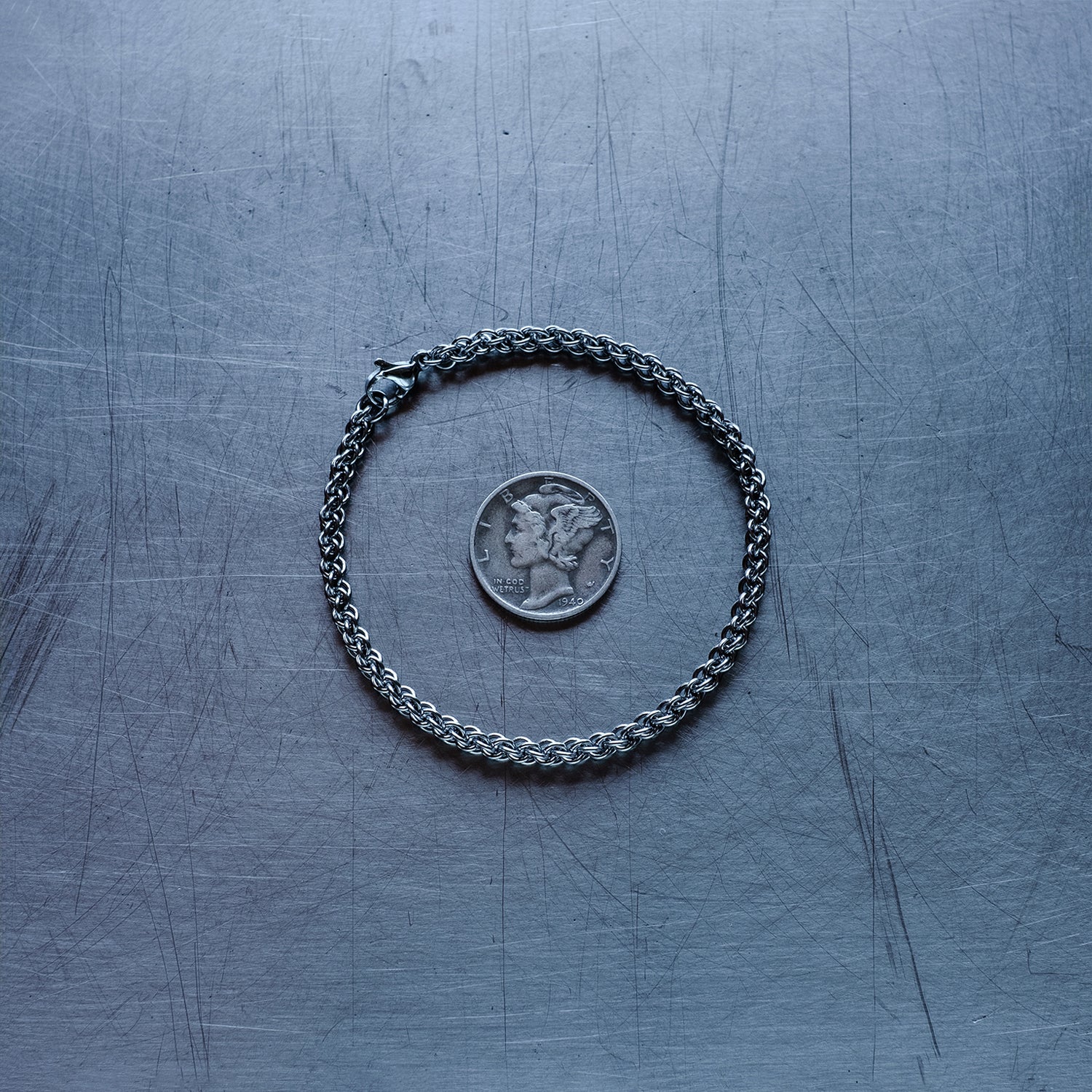 fine jpl3 weave chain bracelet made with 304 stainless steel on a stainless steel surface with a liberty dime for scale