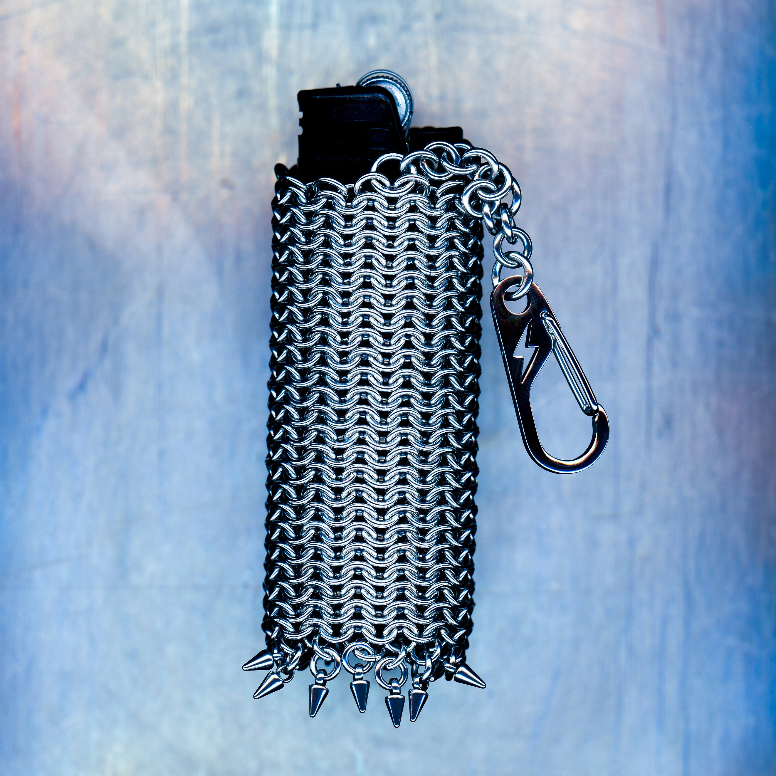 A snug European 4-in-1 chainmaille sleeve for your lighter, finished with dangling spikes that catch the eye. Made with 304 stainless steel. Hangs elegantly from a short chain with a lightning bolt clasp.