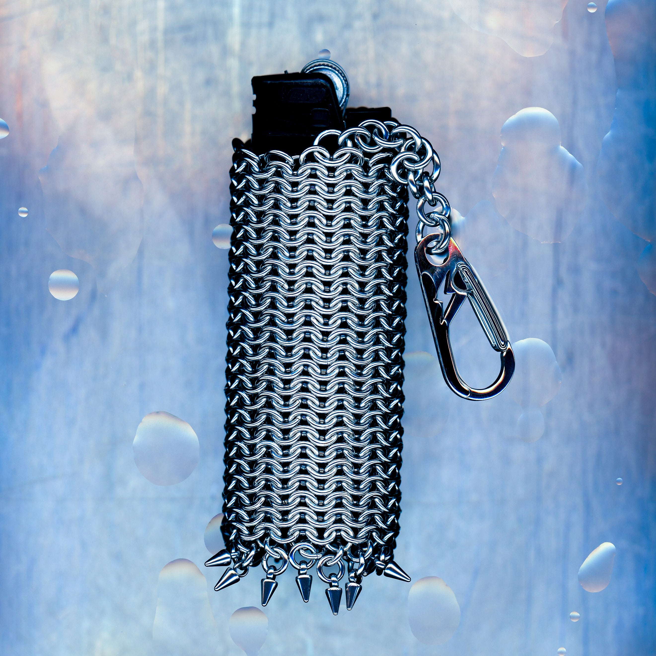 A snug European 4-in-1 chainmaille sleeve for your lighter, finished with dangling spikes that catch the eye. Made with 304 stainless steel. Hangs elegantly from a short chain with a lightning bolt clasp.
