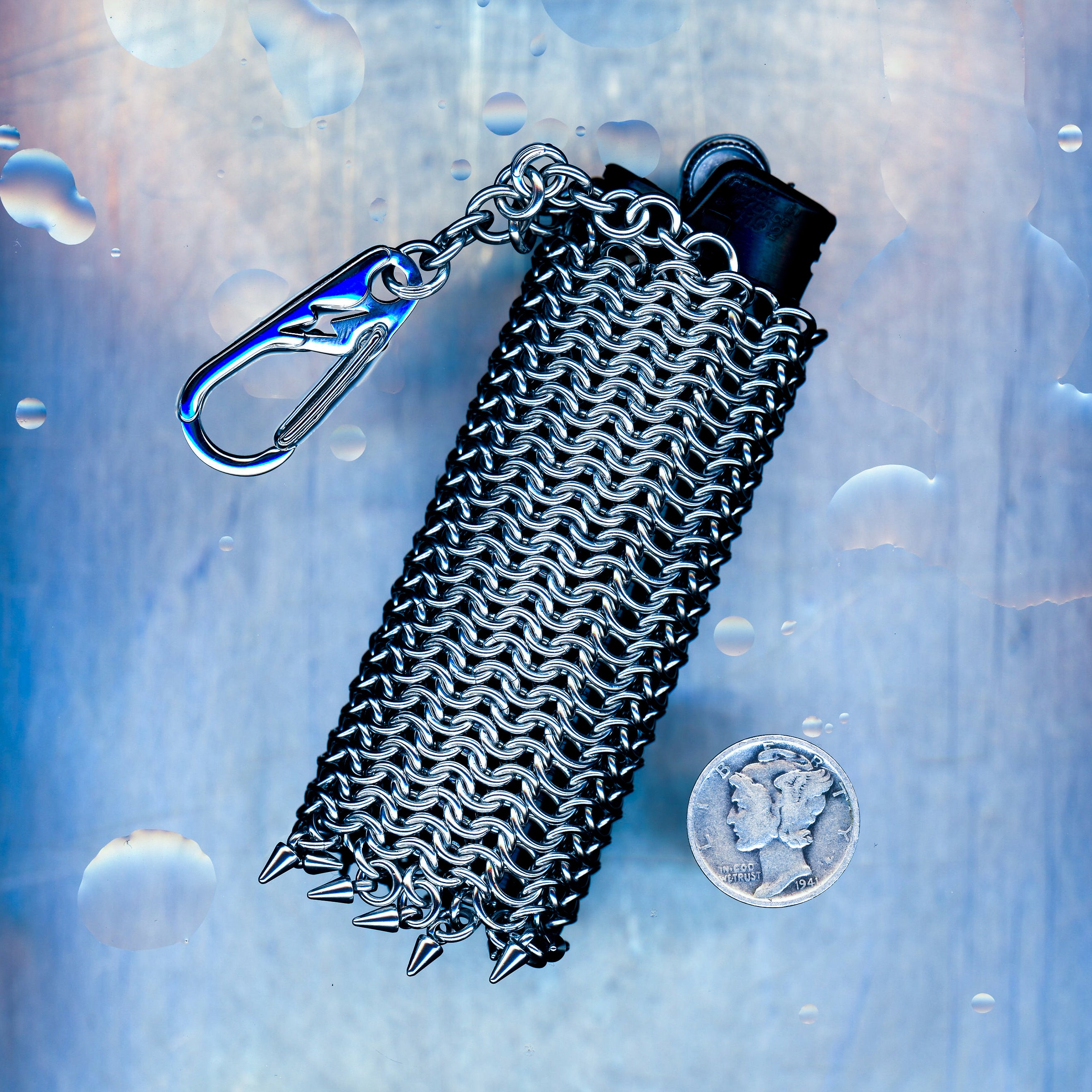 A snug European 4-in-1 chainmaille sleeve for your lighter, finished with dangling spikes that catch the eye. Made with 304 stainless steel. Hangs elegantly from a short chain with a lightning bolt clasp.