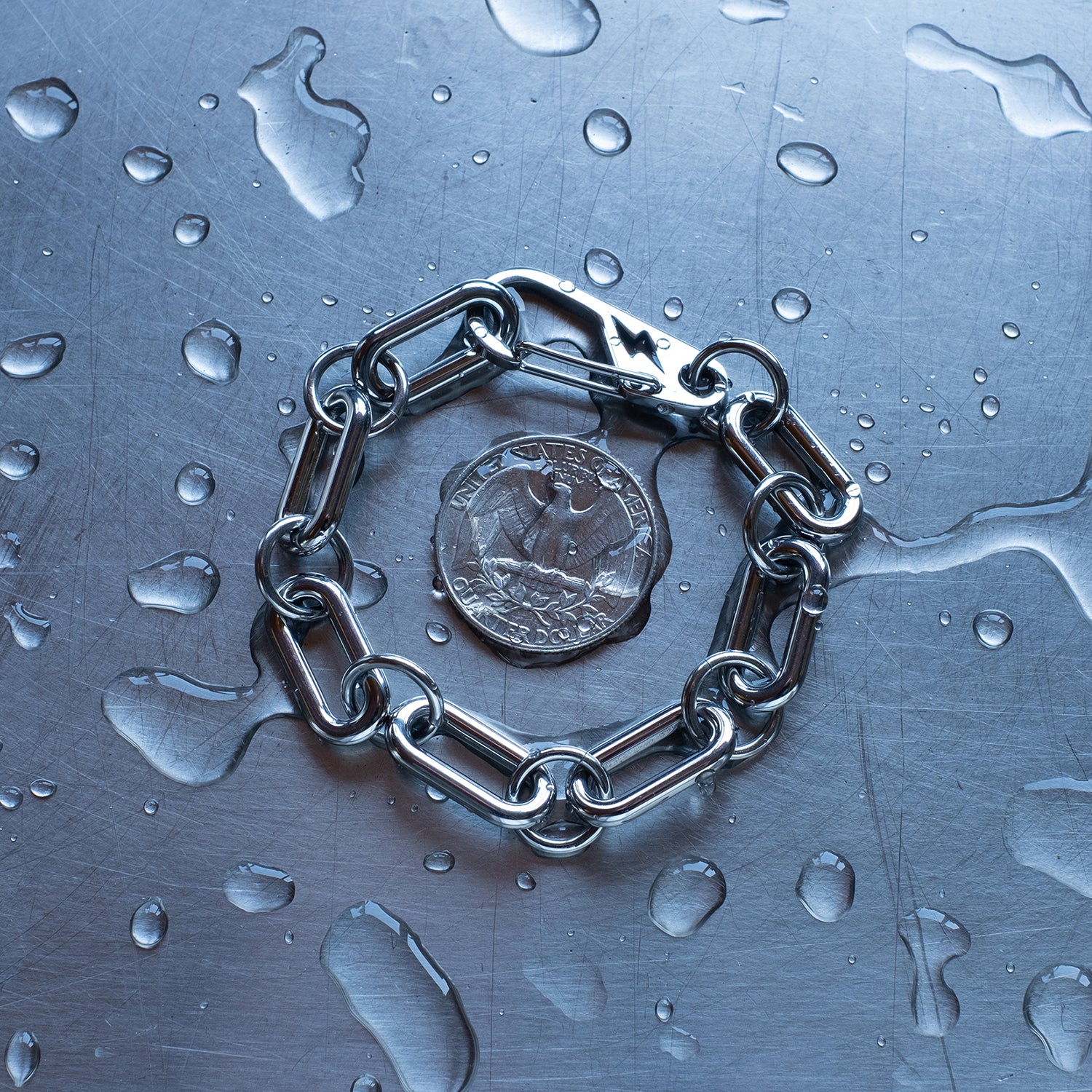 Statement, chunky Oval chain link connected by large round jump rings bracelet featuring a carabiner clasp with a lightning bolt cutout made with stainless steel on a wet stainless steel surface with a quarter for scale